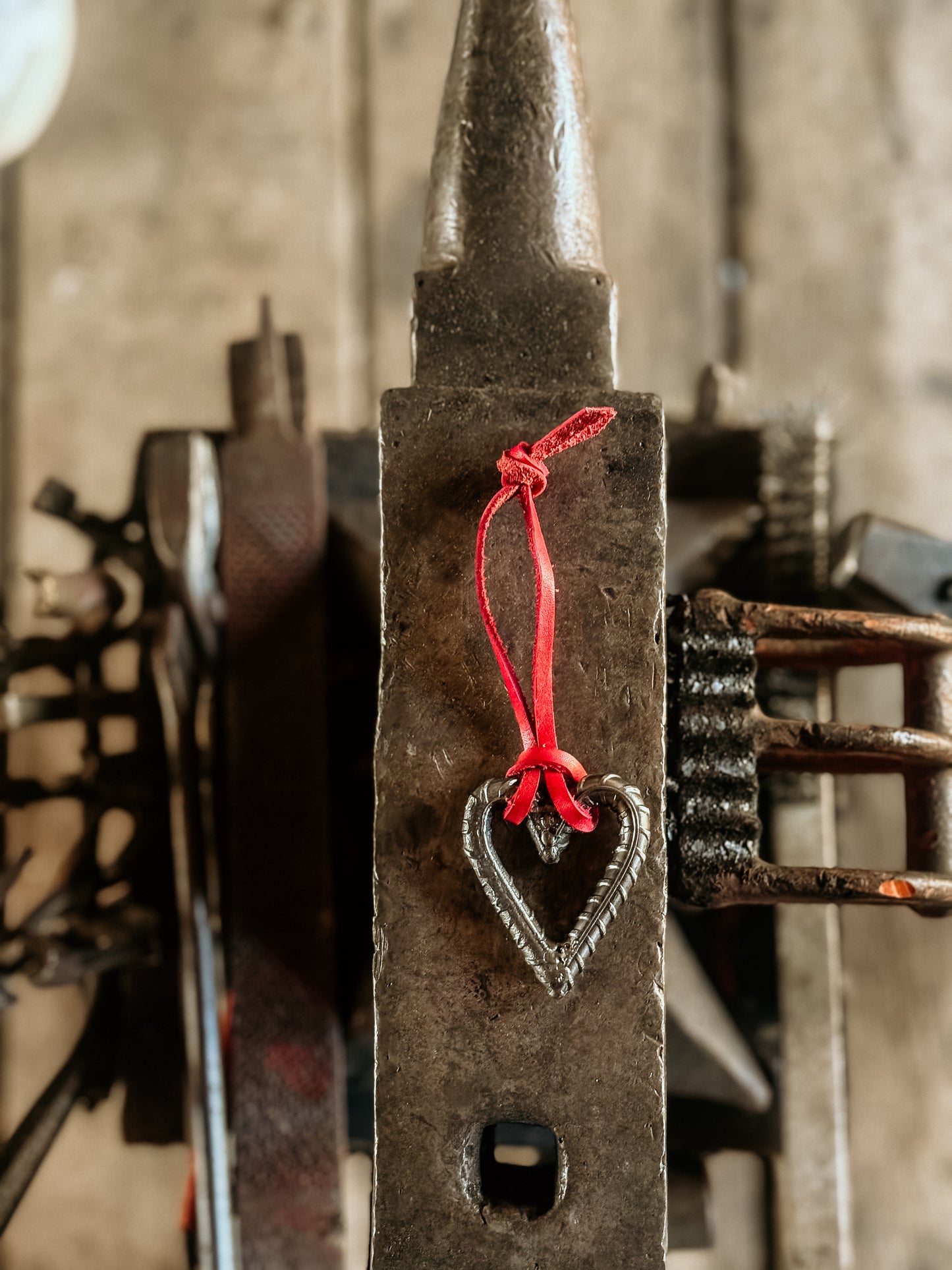 Rustic metal blacksmith forge with a heart-shaped charm and red leather string, blurred background