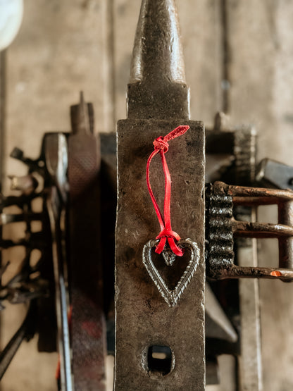 Rustic metal blacksmith forge with a heart-shaped charm and red leather string, blurred background