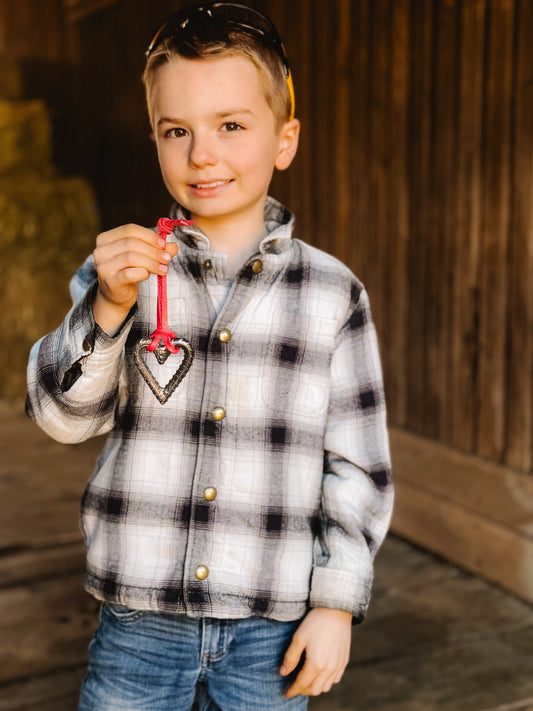 Young boy in a plaid shirt holding a red heart-shaped object in front of a wooden background